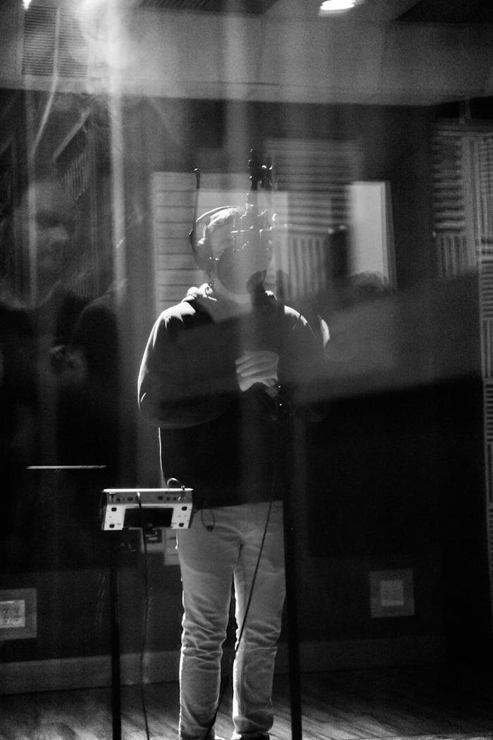 Moody black and white photo of a man singing into a microphone in a recording studio.